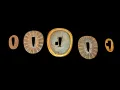 Five-piece kaiguntō tsuba set laid out on a black ground: outer spacers, two rayed seppa, central tsuba