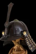 The helmet in profile, showing the brown-lacquered bowl, the tall ken maedate and a gilt crest on the turnback