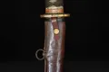 The upper saya with its single suspension ring and brass retaining stud, below the fuchi and brown ito
