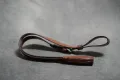 Brown leather reproduction NCO sword knot shown full length, coiled on a grey ground