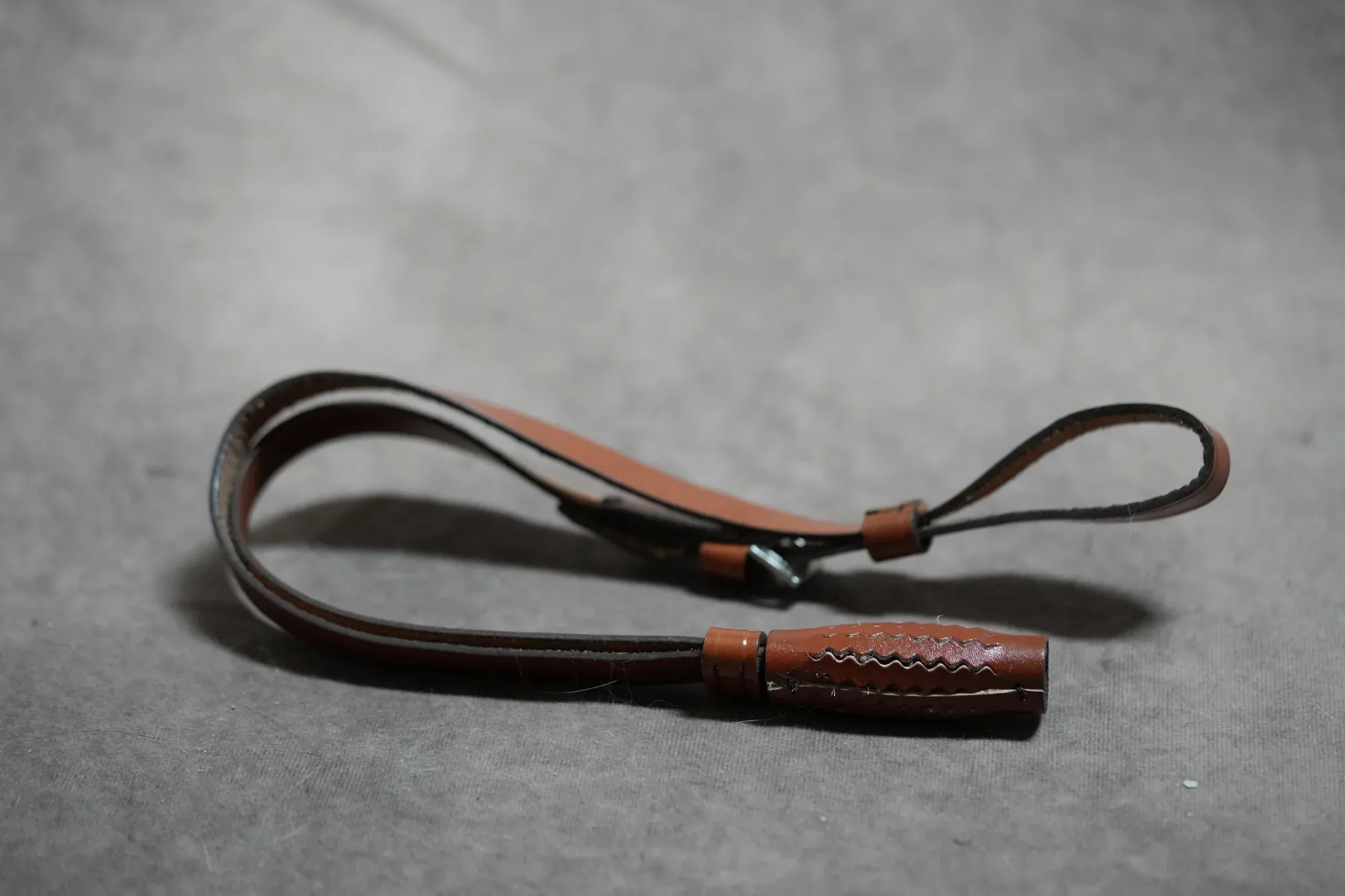 Brown leather reproduction NCO sword knot shown full length, coiled on a grey ground