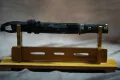 Shōwa-era tantō mounted in black-lacquer aikuchi koshirae, displayed on a stand