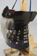 The face armour in profile with the nose lifted away, showing the red lacquer beneath and the full length of the moustache