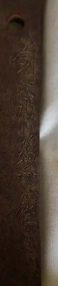 The tang, held upright, showing the worn four-character signature that appears to read Nōshū Kanemichi, with two mekugi-ana
