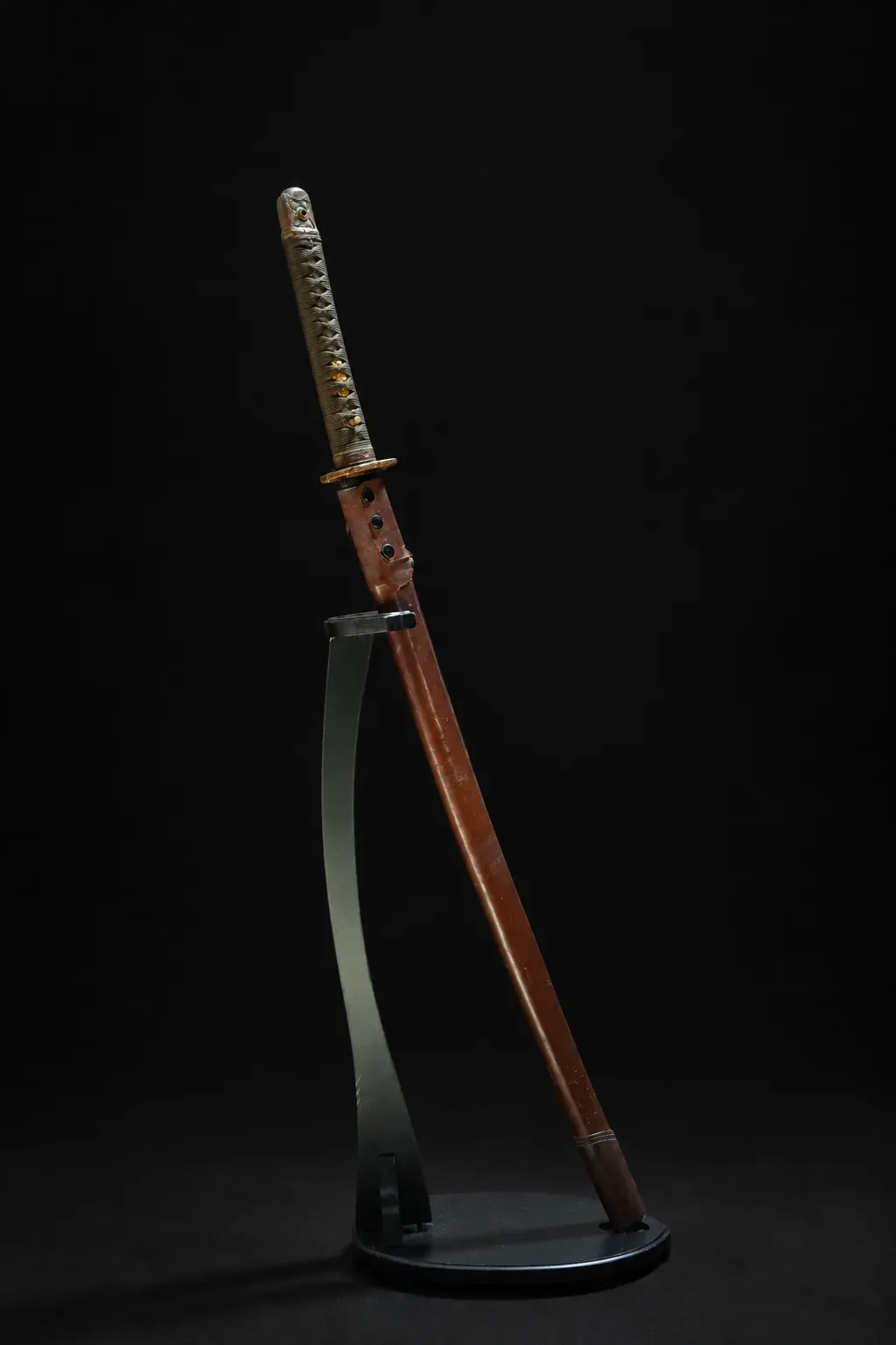 The complete koshirae displayed upright on a stand — same-wrapped tsuka, brass fuchi, and brown leather saya cover