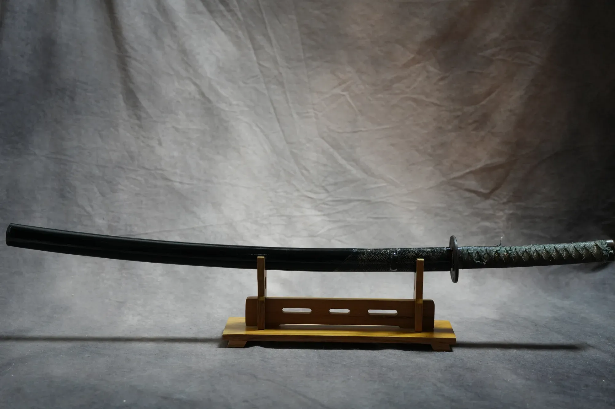 The mounted katana on a stand in its black scabbard with teal-wrapped grip