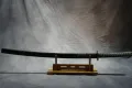 The mounted katana on a stand in its black scabbard with teal-wrapped grip