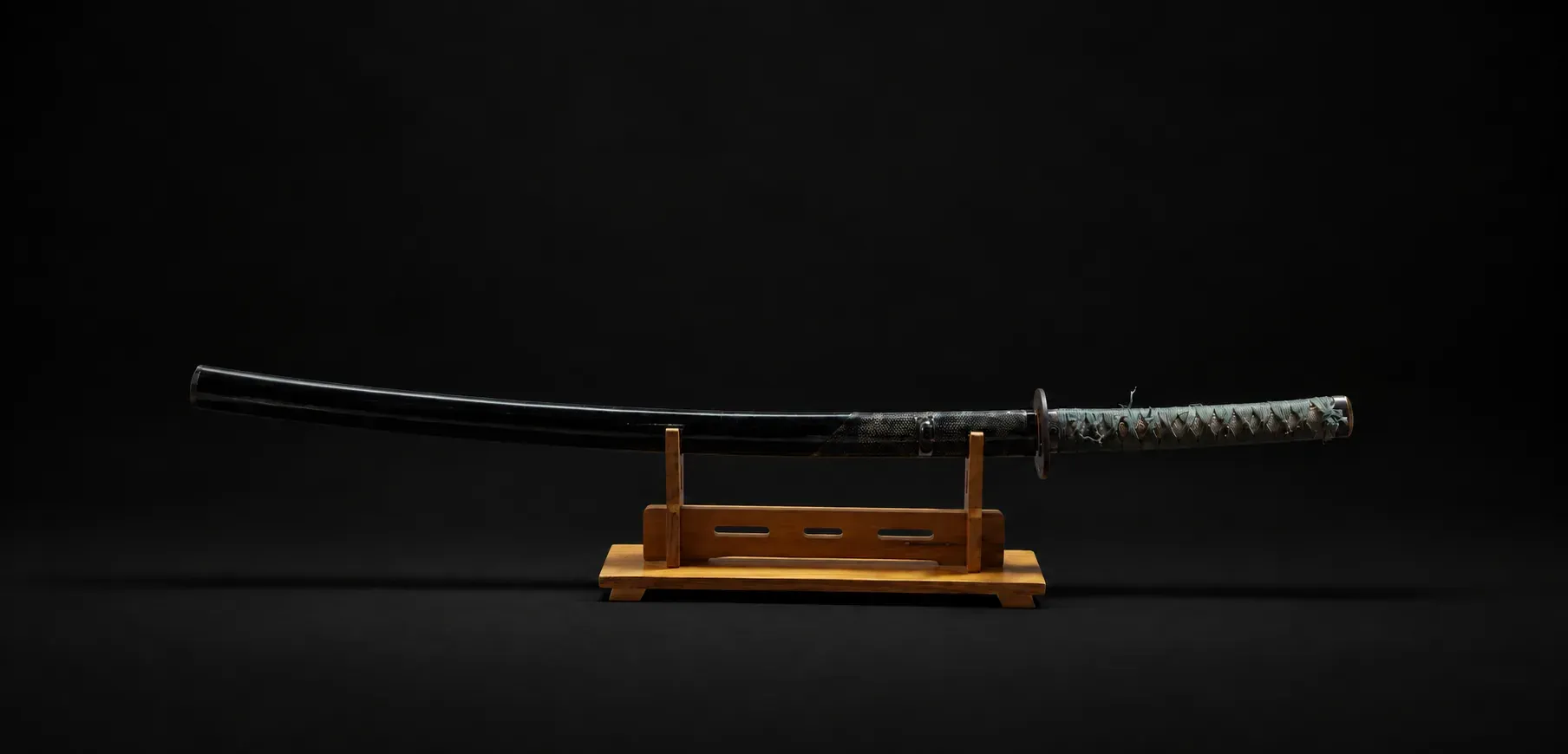 The katana mounted in its black saya on a display stand, the full koshirae with its teal-wrapped grip