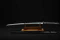 The bare blade on its wooden stand with the black saya laid below it