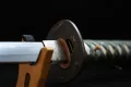 The habaki (blade collar) and copper seppa seated against the tsuba, with the teal tsuka-ito behind