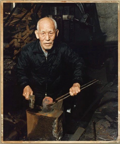Ishidō Teruhide (Kikuchi Seiichi) at his forge, working steel on the anvil